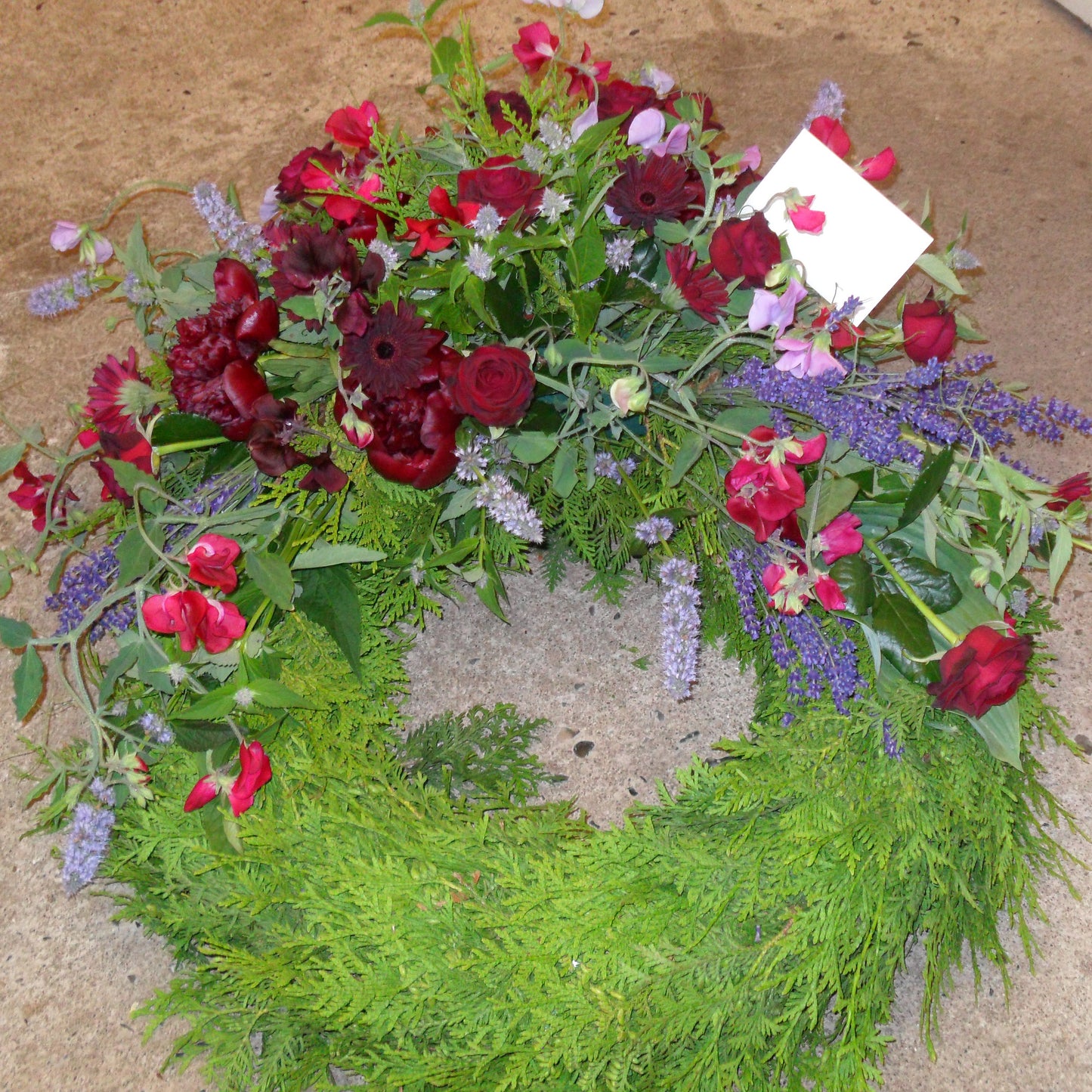 Begravelsesbinderi. Thujakrans med dekoration i røde nuancer.