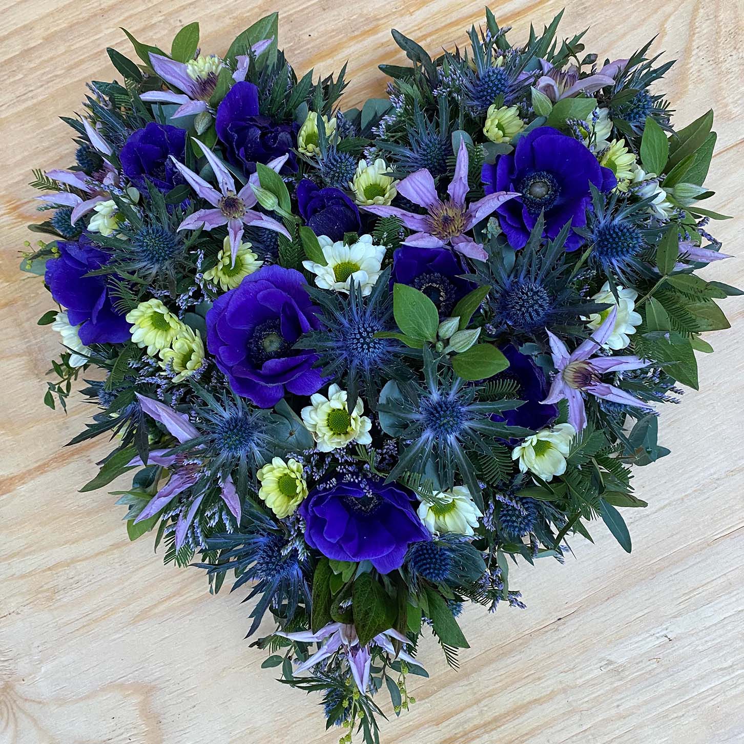 Hjerte dekoreret med afskårne blomster i blå nuancer. Begravelsesbinderi.