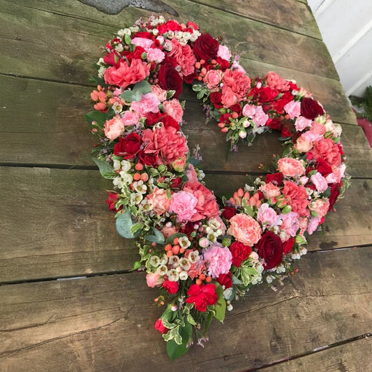 Rundpyntet, åbent hjerte i røde nuancer. Begravelsesbinderi.