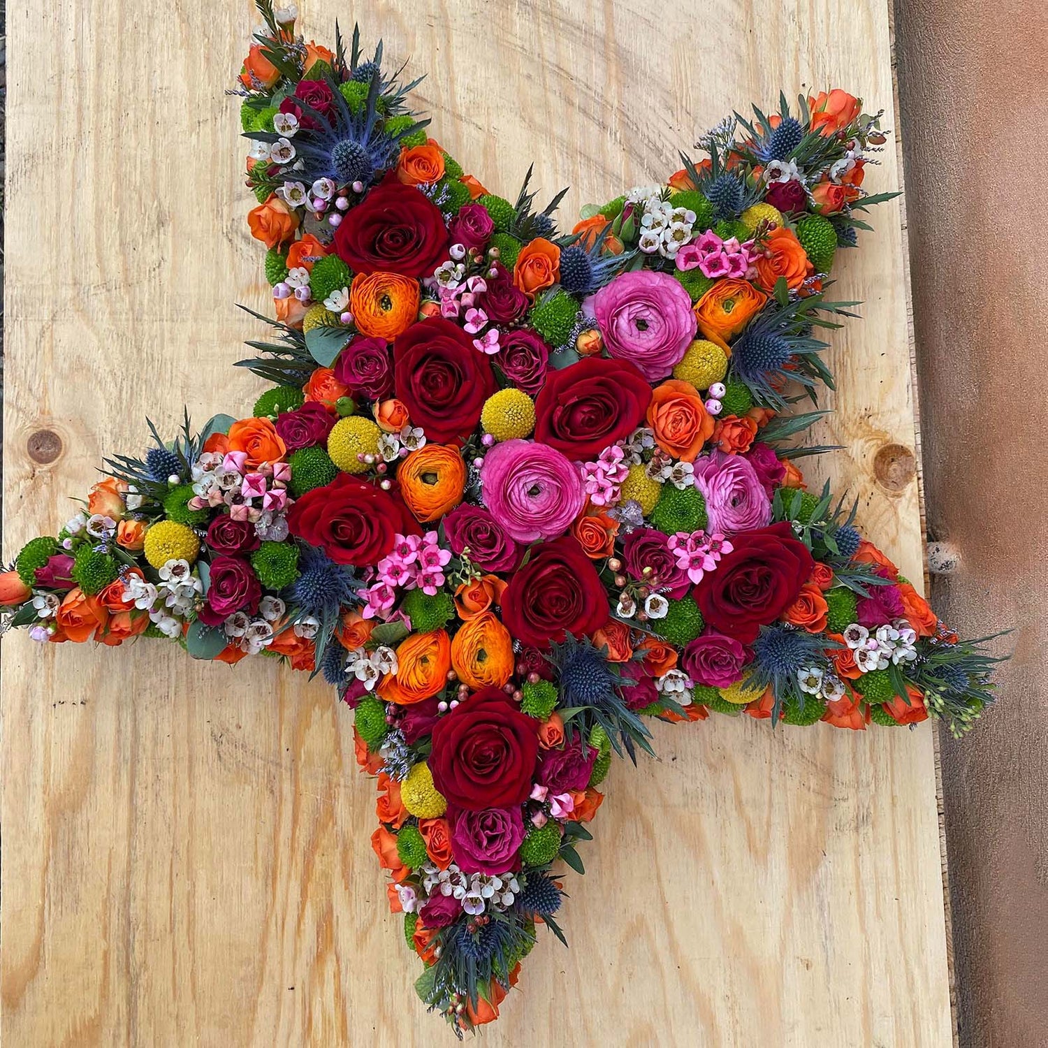 Båredekoration formet som stjerne. Dekoreret med afskårne blomster i klare farver. Begravelsesbinderi.