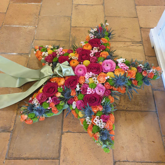 Båredekoration formet som stjerne med bånd. Dekoreret med afskårne blomster i klare farver. Begravelsesbinderi.