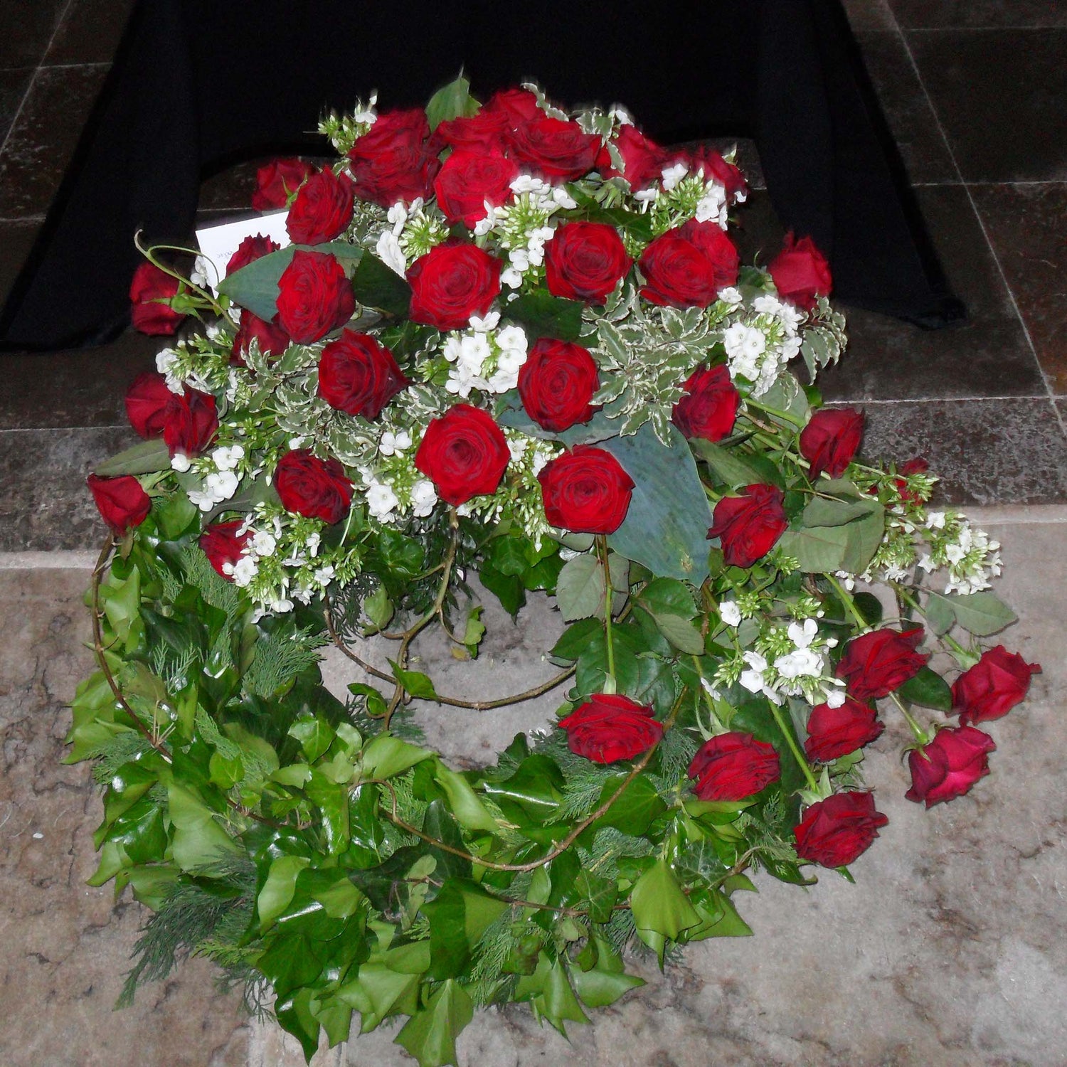 Begravelsesbinderi. Thujakrans med efeu og dekoration i røde/hvide nuancer, hovedsageligt røde roser.