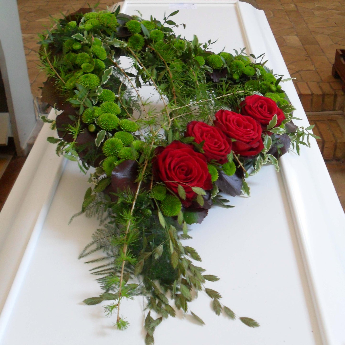 Åbent hjerte i grønne nuancer med fire røde roser. Begravelsesbinderi.