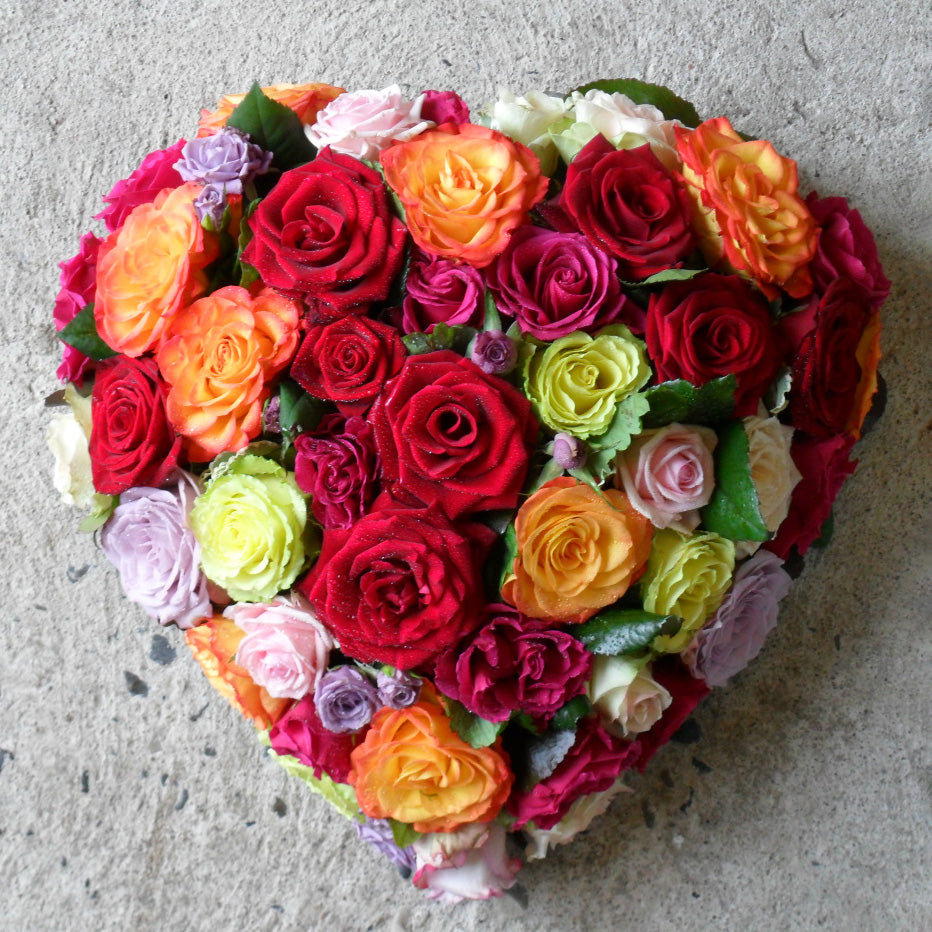 Hjerte dekoreret med roser i forskellige nuancer. Begravelsesbinderi.
