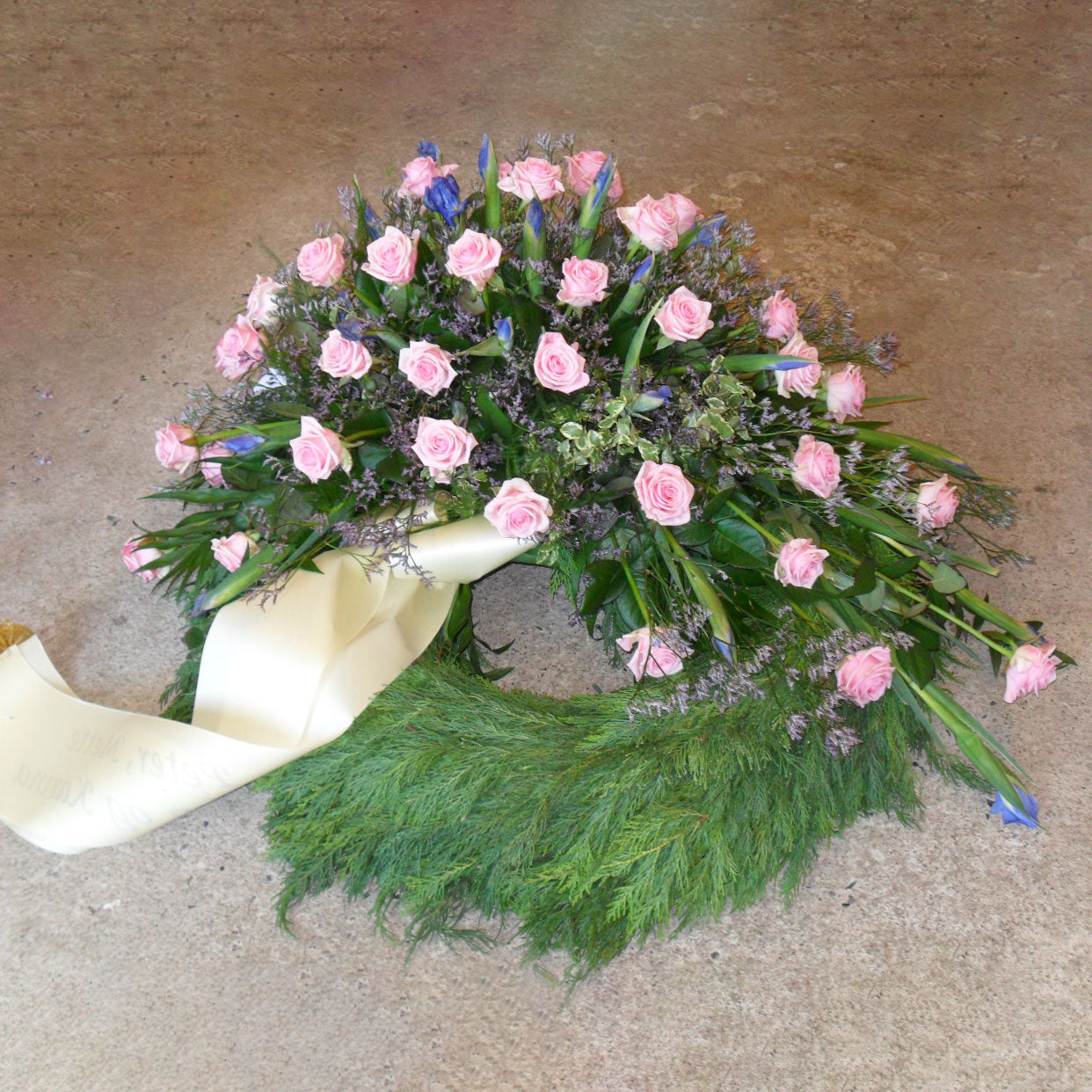 Begravelsesbinderi. Thujakrans med lyserøde roser og blå iris samt et bånd