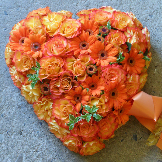 Hjerte med bånd. Hjertet er dekoreret med blomster i orange nuancer. Begravelsesbinderi.